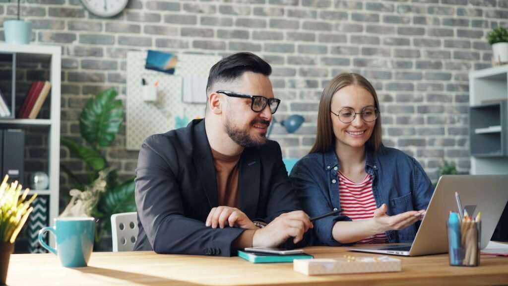 Professional couple smiling and collaborating on a laptop at a modern office table.